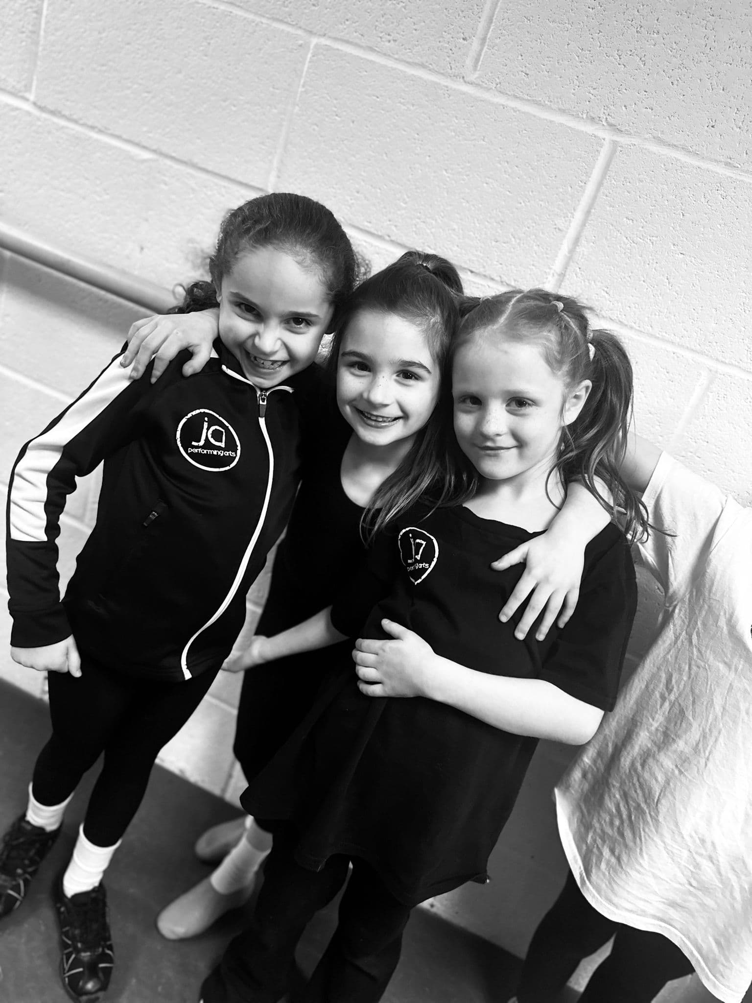 Three young dancers hugging in their JA uniforms